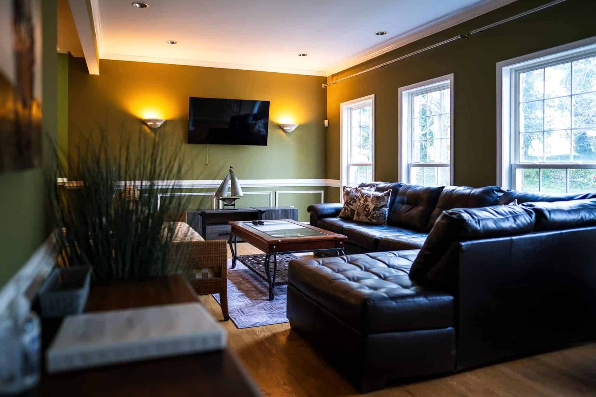 The green common room with a leather sectional and television at the Arnold home